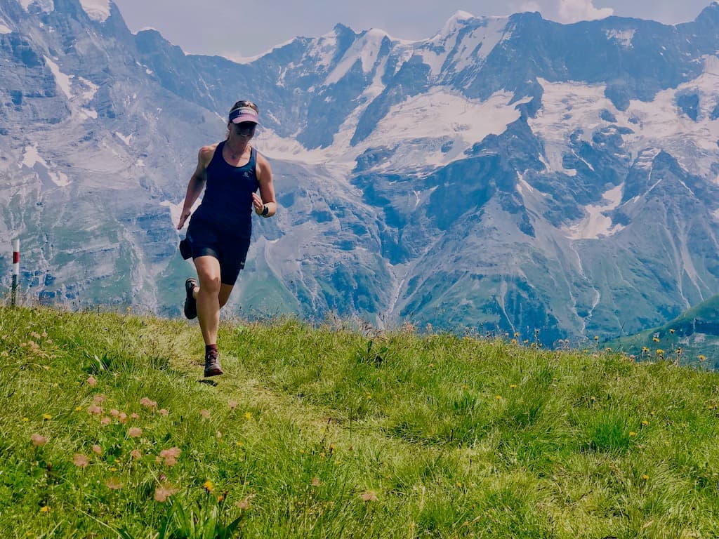 Becki Penrose running on green grass with mountains and glaciers at the backand.