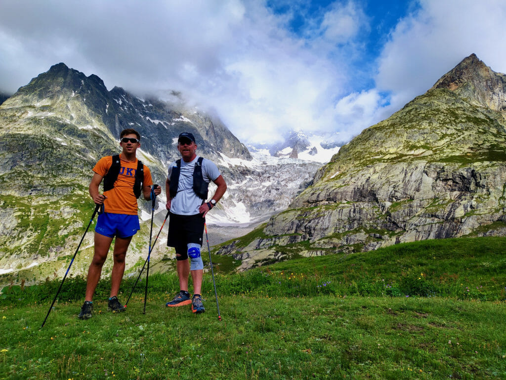 Two trail runners stopped with mountains in background.