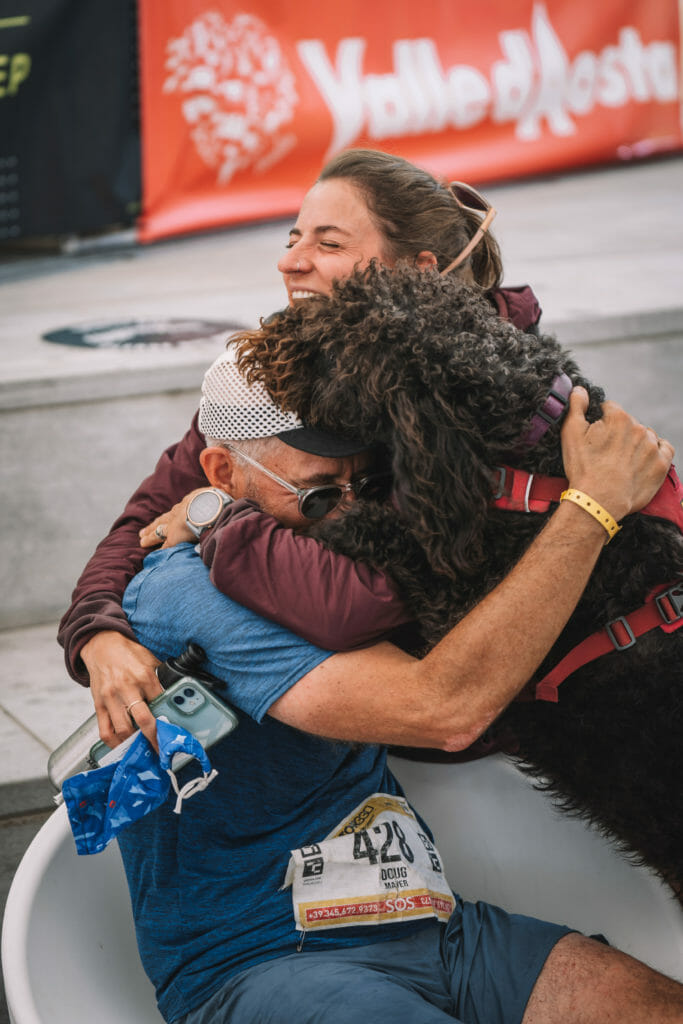 Trail runner Doug Mayer, labradoodle and spectator Hillary Geraldi in a group hug
