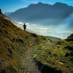 One trailrunner on a single track with mountains and a little lake and sunrays