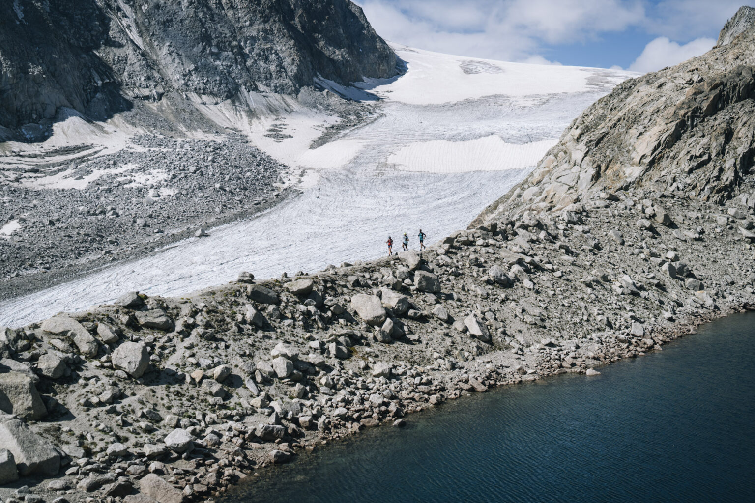 3 runners in distance silhouetted agains large glacier