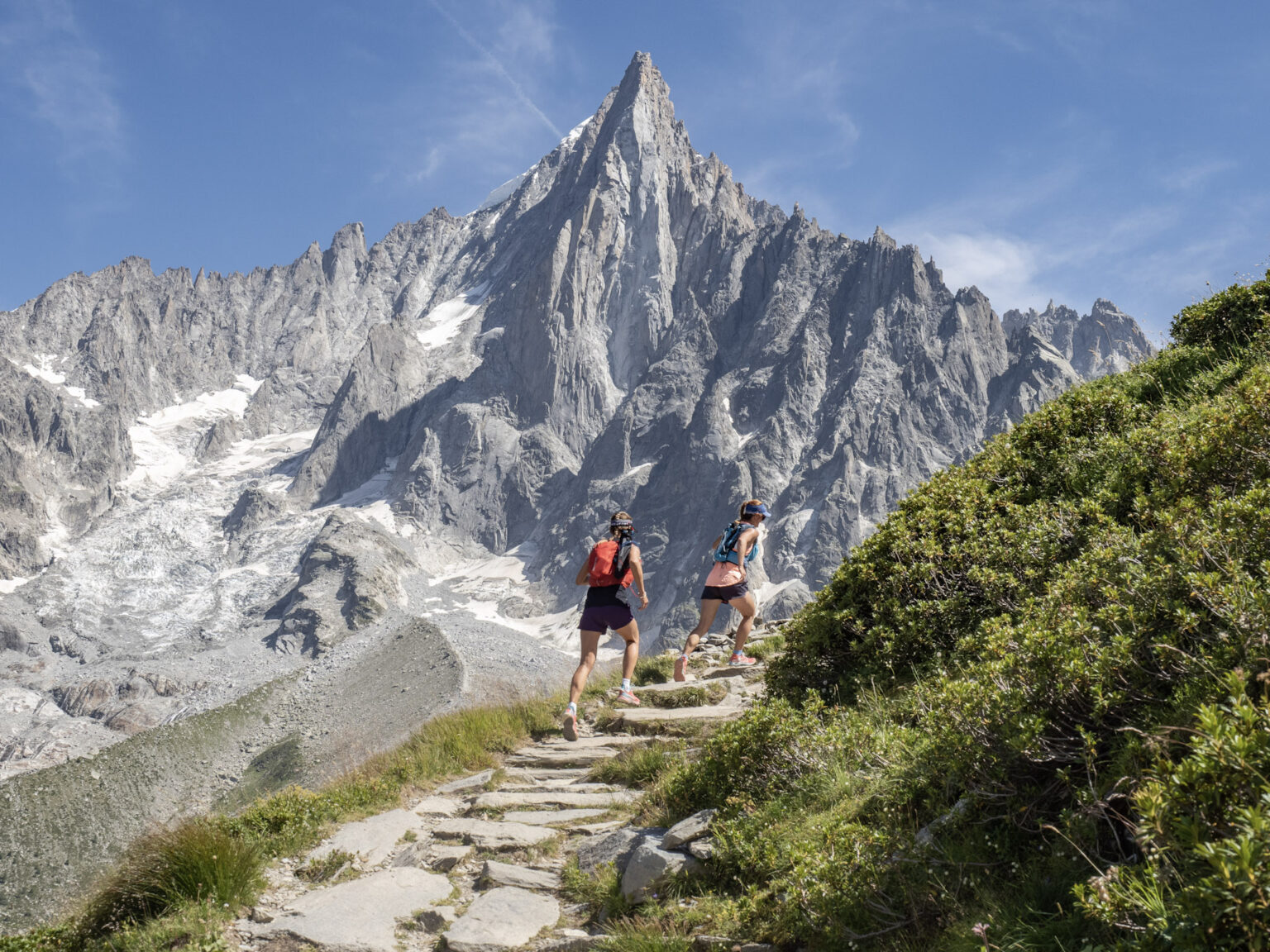 to runners run uphill on Rocky Trail with pointy Rocky Mountain behind