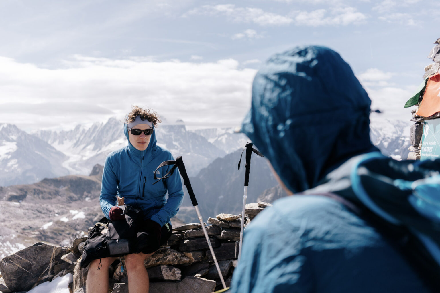 to runners sit on top of Rocky Summit with Alpine mountains in the background