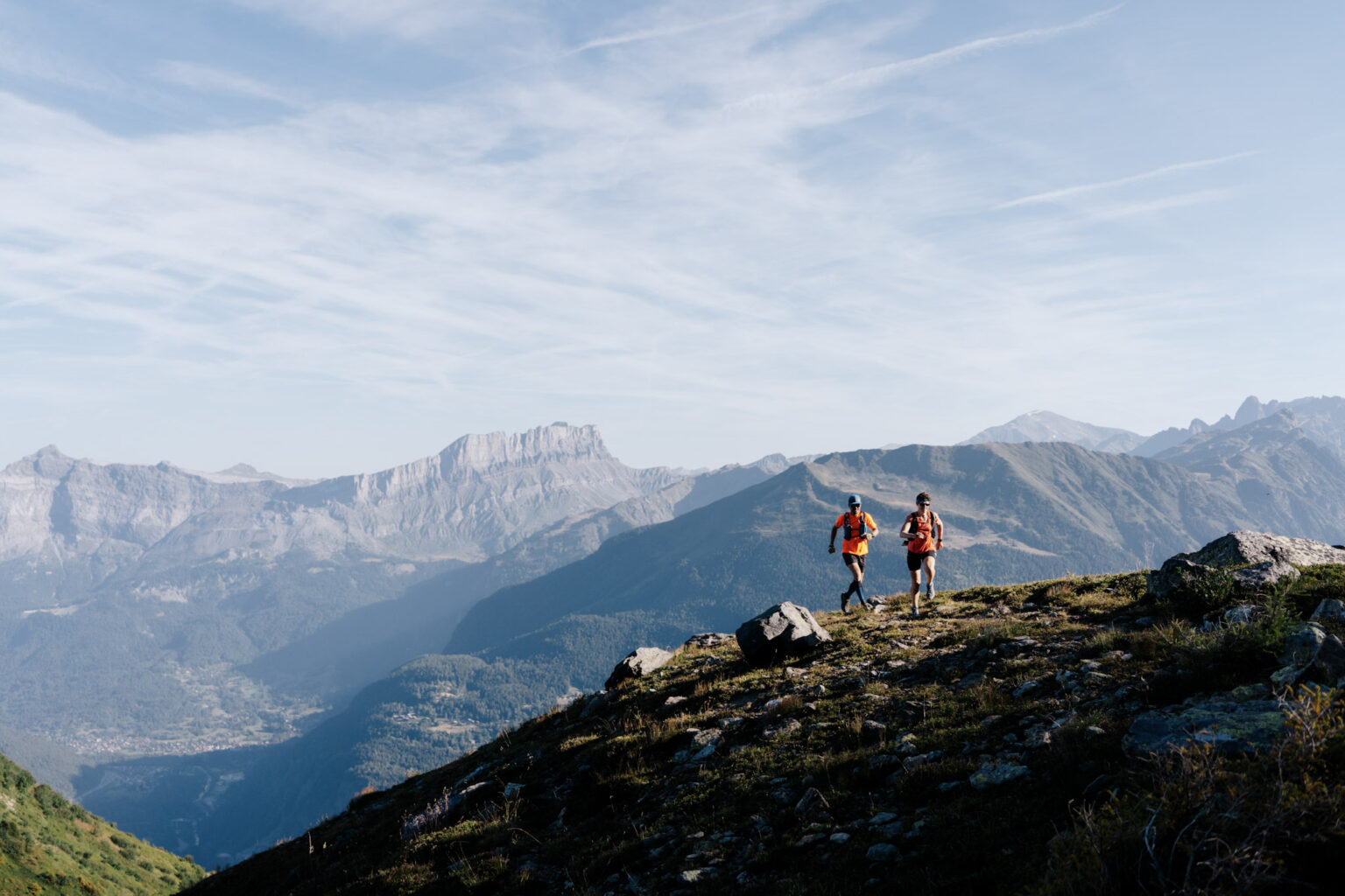 2 runners run up the trail with mountains in background